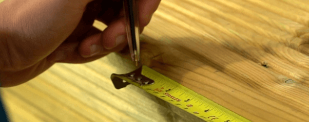 A pencil that is marking a measurement into the wood next to the tape measure.
